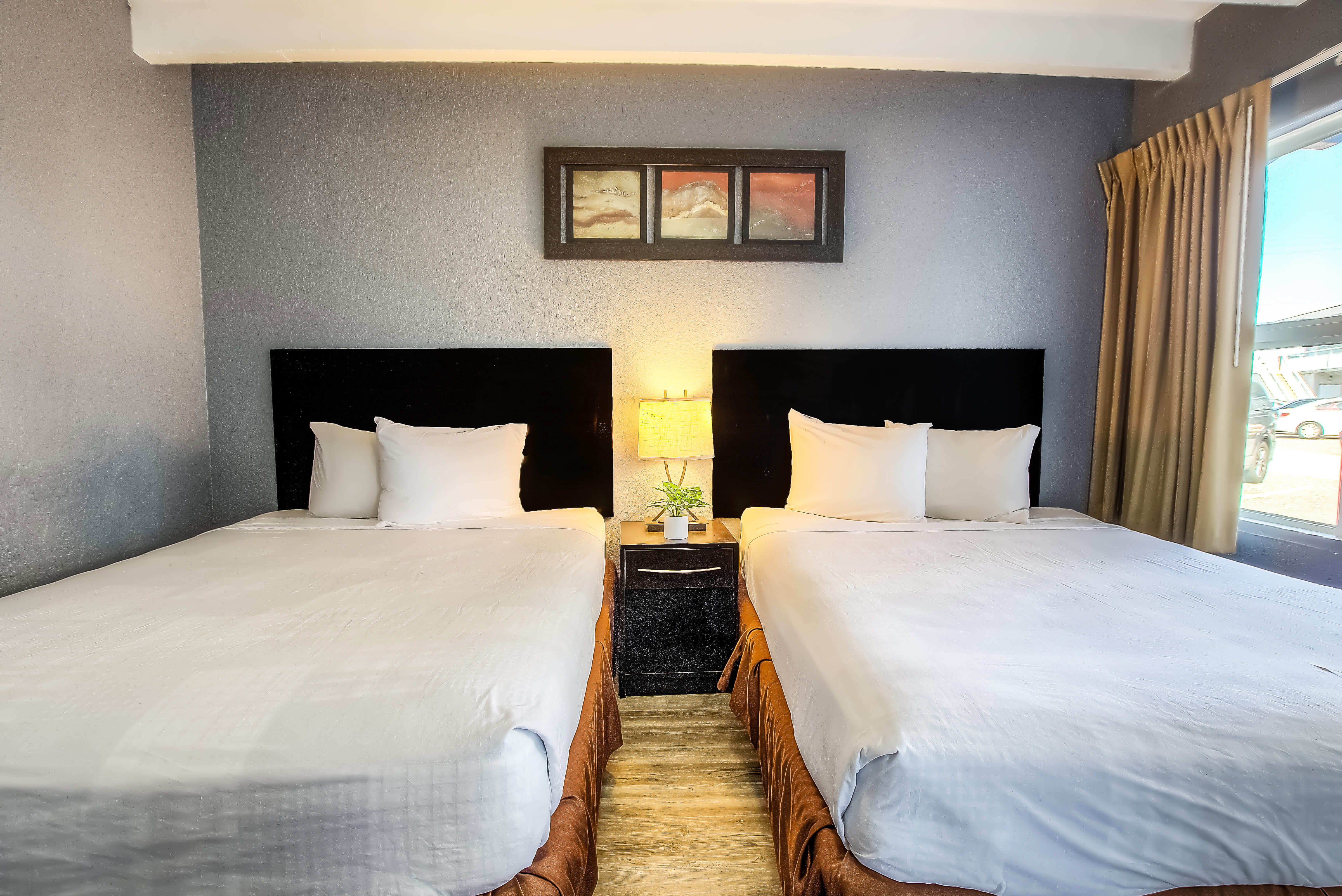 A hotel room with two beds, a nightstand, and a window.