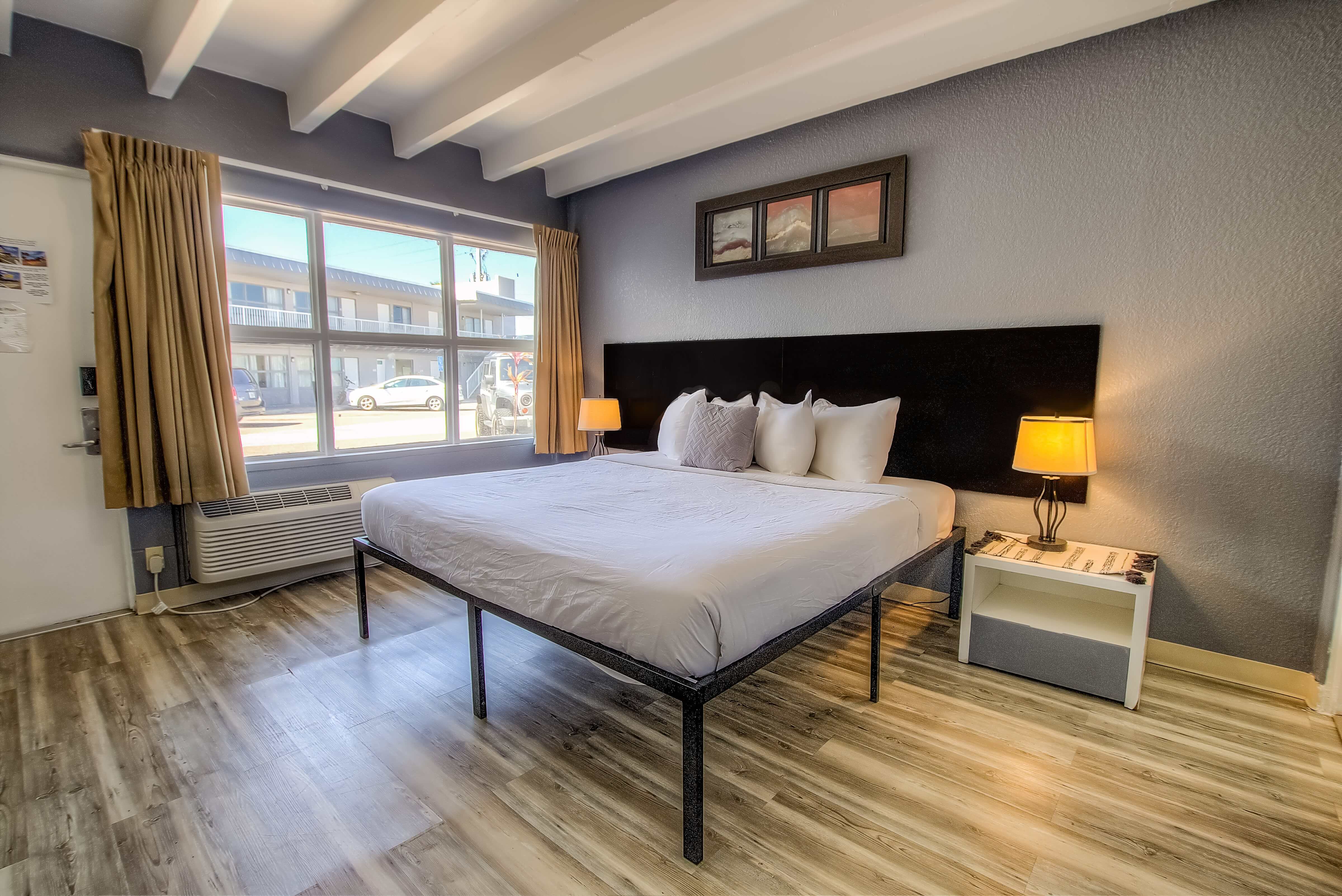 A wide view of a hotel room with a large bed, two nightstands with lamps, and a window.