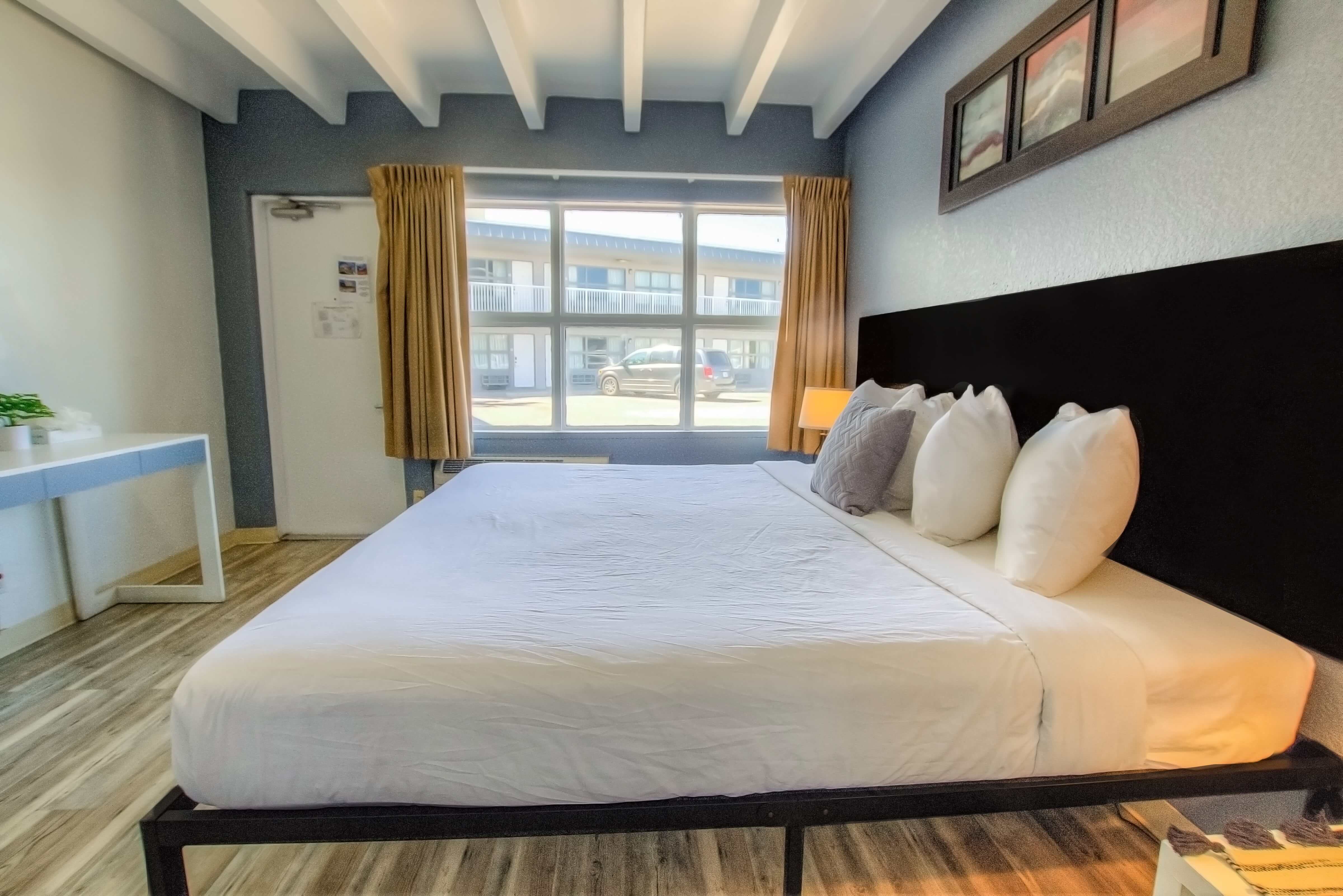 A wide view of a guest room with a large bed, window, desk, and artwork.